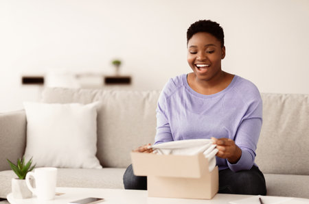 Happy black woman unpacking clothes after online shoppingの写真素材