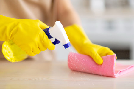 Unrecognizable maid in rubber gloves cleaning countertop at kitchen, closeup of hands with detergent...