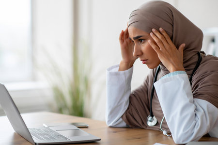 Exhausted female doctor sitting at workdesk in clinicの写真素材