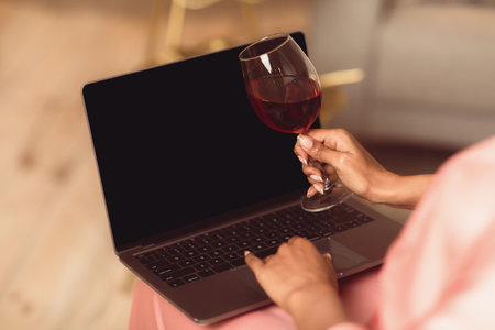 Black woman using laptop with empty mockup screen, drinking wineの写真素材