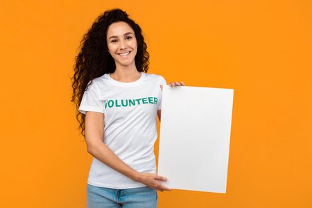 Female Volunteer Holding Empty Paper Board Over Yellow Backgroundの写真素材