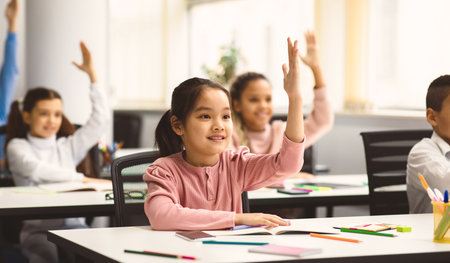 Diverse group of little school children raising hands at classroom