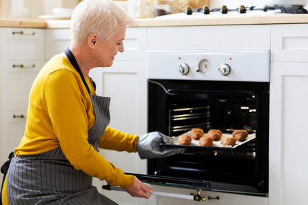Joyful grandmother taking homemade croissants out of ovenの写真素材