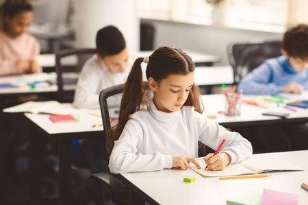 Portrait of small girl sitting at desk writing or drawingの写真素材