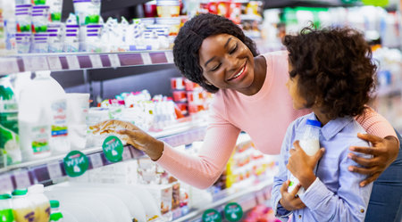 Positive young black mom teaching her daughter how to choose dairy products at grocery storeの写真素材