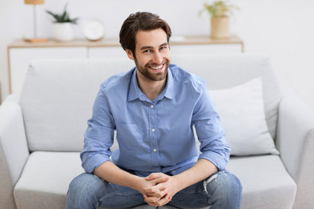 Guy Sitting On Sofa Smiling To Camera Posing At Homeの写真素材