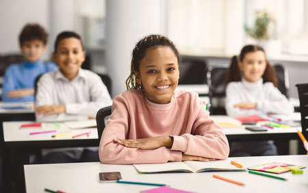 Portrait of small black girl sitting at desk in classroom