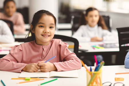 Portrait of small asian girl sitting at desk in classroom