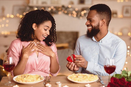 Smiling black man making proposal with ring to his fiance