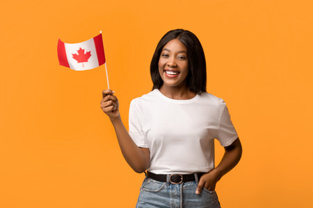 Happy black woman showing canadian flag on orangeの写真素材