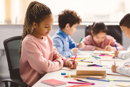 Smiling african american schoolgirl sitting at desk drawing picture