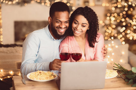 Black couple having videocall using laptop drinking wineの写真素材