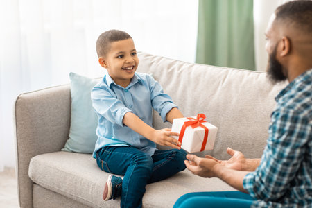 African Boy Giving Birthday Gift To Father Sitting At Homeの写真素材