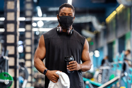 African muscular man wearing protective mask while exercising at gymの写真素材