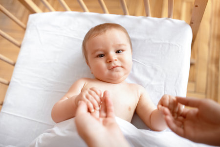Beautiful little baby laying in cot, holding moms handsの写真素材
