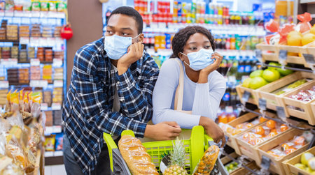 Black family in face masks buying food, tired of shopping for groceries at supermarket during covid-19 outbreakの写真素材