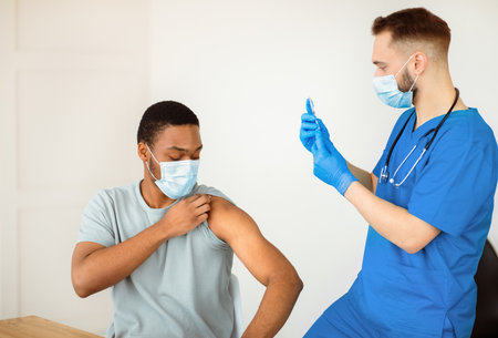 Covid-19 vaccination program. Black male patient getting coronavirus vaccine shot on visit to physician at health centreの写真素材