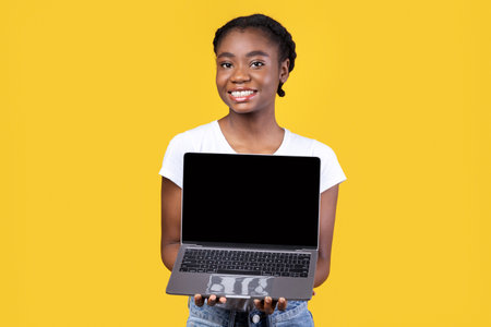Black Lady Showing Laptop Screen Holding Computer On Yellow Backgroundの写真素材