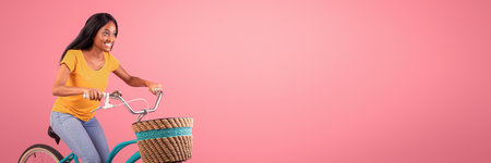 Portraif of pretty black lady riding vintage bicycle on pink studio backgroundの写真素材