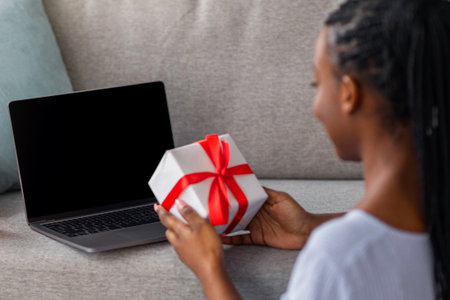 Black lady with dreadlocks holding present, using laptop