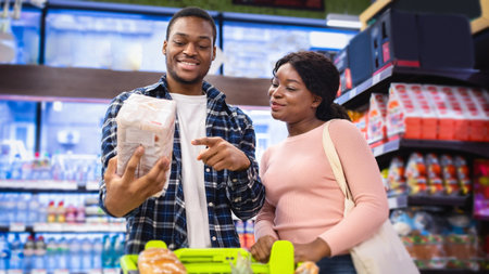 Attractive black woman and her husband shopping for groceries at supermarket, choosing products of best qualityの写真素材