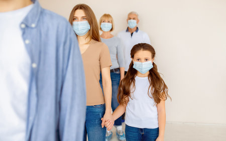 Parent and child in medical masks waiting in line for coronavirus vaccination at clinicの写真素材