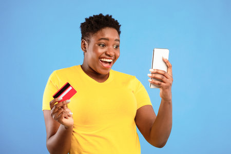 Excited African Woman Using Smartphone And Credit Card, Blue Background