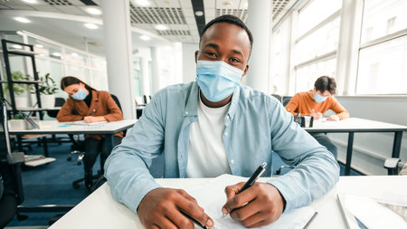Black male student in mask sitting at desk in class