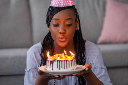 Pretty young black birthday lady blowing candles on cakeの写真素材