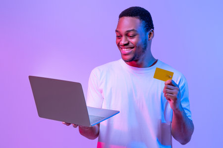 Online Payments. Happy african male with credit card and laptop, neon lightの写真素材
