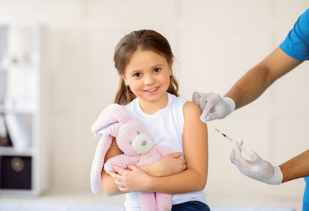 Happy little girl with toy bunny getting coronavirus vaccine injection at hospital. Healthcare and...