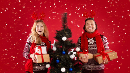 Portrait of happy young couple with Christmas tree and gifts over red backgroundの写真素材