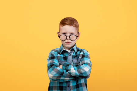 Angry boy in eyeglasses with arms crossed on yellow