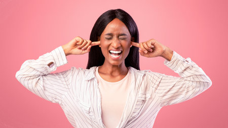Portrait of irritated young black woman closing ears with fingers and shutting her eyes on pink...