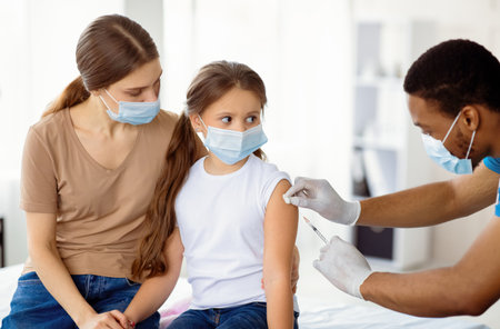 Mother and daughter in medical masks getting vaccinated against covid-19, doctor giving injection of coronavirus vaccineの写真素材