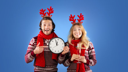 New Year celebration. Young couple with champagne and clock showing five minutes till midnight, blue...