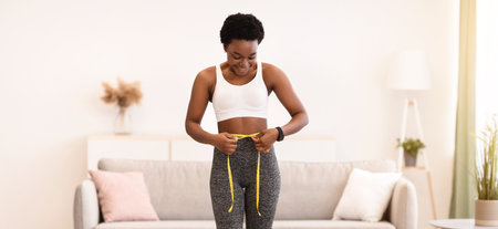Joyful Black Female Measuring Waist Standing On Scales At Homeの写真素材