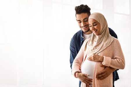 Loving arab man hugging his pregnant muslim wifes belly at home