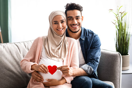 Happy Expectation. Muslim Couple Holding Red Paper Heart Near Womans Pregnant Bellyの写真素材