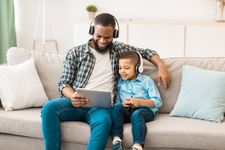 African Father And Kid Wearing Headphones Using Tablet At Homeの写真素材