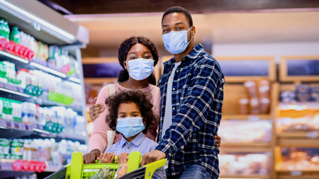 Young black family with child wearing face masks while shopping for groceries at supermarket during...