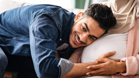 Happy Father. Joyful middle eastern man listening his pregnant wifes tummy, croppedの写真素材