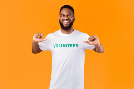 Volunteer guy pointing fingers at himself posing on yellow background