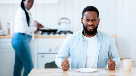 Starving Angry Black Man Waiting For Food At Table In Kitchenの写真素材