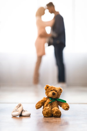 Teddy Bear And Small Baby Shoes With Blurred Pregnant Couple On Backgroundの写真素材