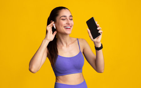Smiling Young Woman In Sportswear Listening To Music Holding Cellphoneの写真素材