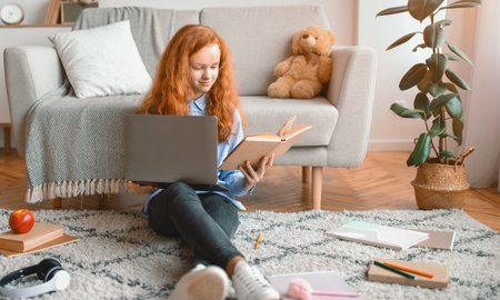 Girl sitting on the floor, reading book, using laptop computer