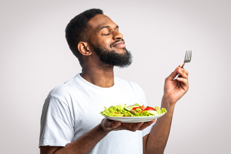 Bearded Black Guy Enjoying Vegetable Salad Standing Over White Backgroundの写真素材