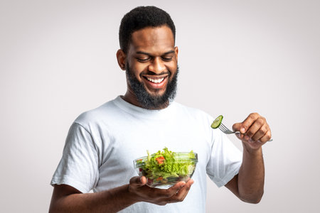 Happy Black Man Eats Fresh Vegetable Salad Over White Backgroundの写真素材