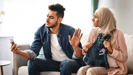 Gadget Addiction. Indifferent arab man using smartphone at home, ignoring pregnant wifeの写真素材